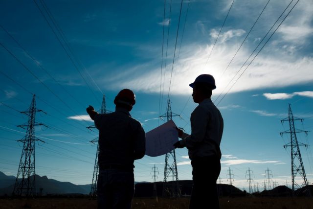 silhouette of two engineers standing at electricity station, discussing plan